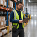 Warehouse worker wearing black Cognex barcode reader sling holster while reviewing a clipboard near inventory shelving.