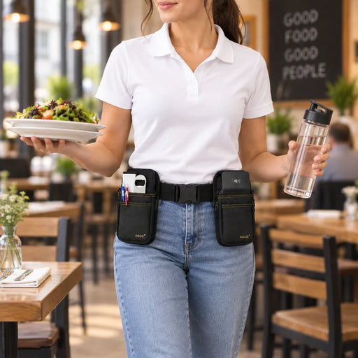 A woman in a white polo shirt and jeans stands in a restaurant holding a plate of salad and a water bottle, wearing a black waist bag with Adyen POS terminal pockets and pens on the front.