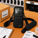Black Honeywell shoulder sling holster on a warehouse workstation with Honeywell handheld computer, pick list, barcode labels, and packing supplies.