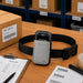 Gray Janam waist belt case displayed on a warehouse pick station with a Janam mobile computer, pick list, barcode labels, and order processing materials.
