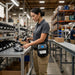 Worker using a handheld scanner at a warehouse workstation while wearing an AgozTech SATO mobile printer waist belt.