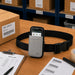 Gray Newland mobile terminal waist belt holster displayed on a warehouse pick station with a Newland device, pick list, barcode labels, and order processing materials.