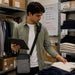 Retail employee wearing gray Agoz Orderman Pulse HT10 crossbody tablet case while checking clothing inventory in a store stockroom.