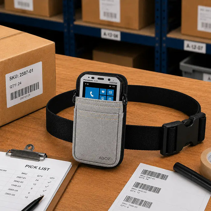 Gray Panasonic Toughbook waist belt pouch displayed on a warehouse pick station with barcode labels, pick sheet, tape, and inventory workflow materials.