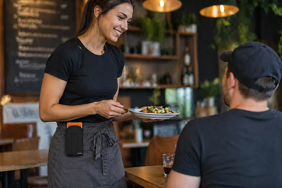 Waitress wearing an AgozTech Sunmi POS handheld terminal holster clipped to her apron while serving food in a restaurant.