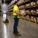 Worker with rugged Zebra Handheld  in a warehouse holding a box, with shelves filled with packages in the background.