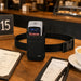 Agoz waist belt carrying case with SpotOn payment terminal displayed on a restaurant table beside menus and a guest check.