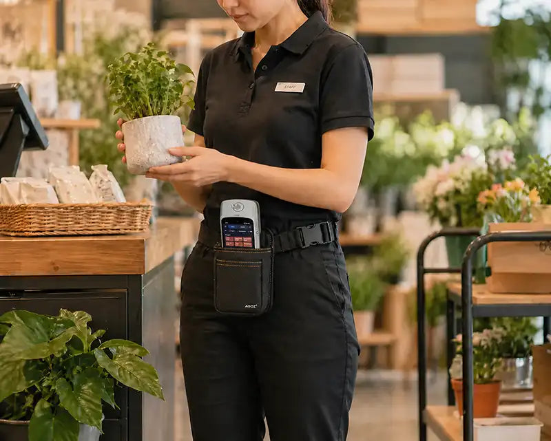 Retail employee carrying a SpotOn payment terminal in an Agoz waist belt case while arranging merchandise in a plant and gift shop.