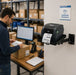 Warehouse employee applying shipping labels near an AgozTech black wall mount printer shelf holding a TSC desktop label printer at a packing station.