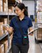 Worker wearing a Unitech shoulder sling holster crossbody while checking barcode labels and inventory paperwork in a warehouse aisle.