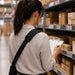 Worker wearing a crossbody shoulder sling holster while reviewing inventory paperwork along warehouse shelving.