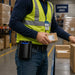 Warehouse logistics worker wearing a black AGOZ belt holster with a Datalogic mobile computer while handling packages in a shipping area.