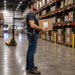 A man with a honeywell mobile computer scanner in a belt holster is carrying a box in a warehouse
