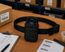 AGOZ black waist case holding a Zebra rugged scanner on a warehouse packing table with a pick list, barcode labels, boxes, and shipping supplies.