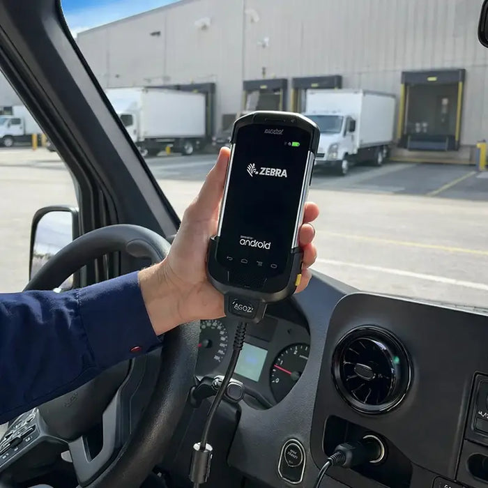 Hand holding Zebra TC77 mobile computer in plugged-in vehicle charger at loading dock