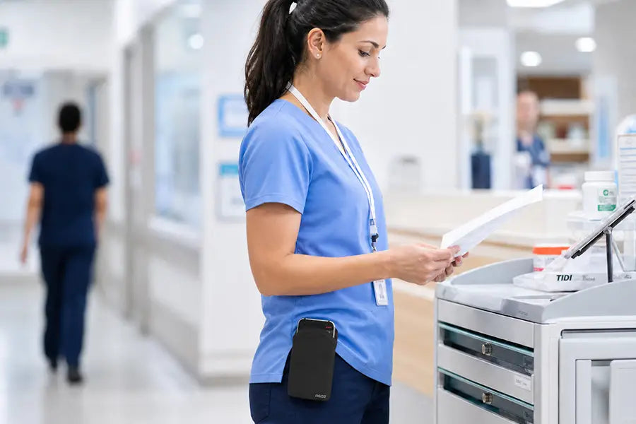 Healthcare worker wearing an Ascom DECT handset case clipped to scrub waistband in a hospital corridor