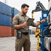 Worker wearing the leather Unitech handheld scanner case on a belt while using a tablet beside industrial equipment in a field operations setting.