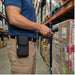 Worker wearing the Newland scanner case with metal belt clip while scanning pallet labels in a warehouse aisle.