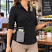 Restaurant server wearing gray Agoz Orderman POS holster with adjustable crossbody sling while carrying a food tray, keeping the payment terminal accessible.