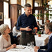 Restaurant server using an iMin M2 POS terminal while wearing an AgozTech belt pouch during table service.