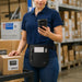 Almex mobile computer utility apron worn by warehouse worker with notepad, pen, and box cutter in front pockets.